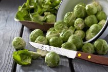 Upturned Bowl of brussels sprouts and knife on grey wooden table — Stock Photo