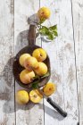 Halved and whole yellow plums and a wooden spoon on white wooden table — Stock Photo