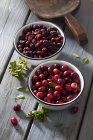 Bowls of dried and fresh cranberries on grey wooden table — Stock Photo