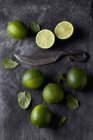 Lime fresche intere e dimezzate con foglie e coltello su tessuto nero — Foto stock