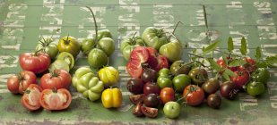 Varieties of fresh tomatoes on green wood — Stock Photo