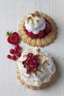 Two meringue tartlets with red currants and strawberries on wood — Stock Photo