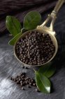 Brass spoon with black peppercorns and leaves on textile, close up — Stock Photo