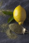 Paleta de latón con pimienta de limón seca granulada con limón fresco y hojas en tela negra - foto de stock
