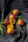 Whole and halved apricots on black fabric with old knife and leaves — Stock Photo