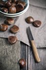 Chestnuts on wooden table and in bowl — Stock Photo