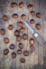 Fresh chestnuts on dark wood with knife — Stock Photo