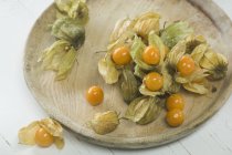 Physalis fruits avec des fleurs séchées sur assiette en bois — Photo de stock