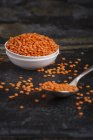 Rote Linsen in kleiner weißer Schüssel und Löffel auf dunkler Oberfläche, Nahaufnahme — Stockfoto