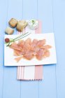 Vue surélevée de l'assiette avec des morceaux de saumon fumé placés sur la serviette à la table en bois bleu — Photo de stock