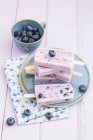 Blueberry yogurt ice lollies on blue plate on wooden table with fresh blueberries — Stock Photo
