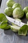 Fresh Brussels sprouts and knife on grey wooden table — Stock Photo