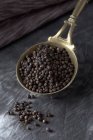 Brass spoon with black peppercorns on textile, close up — Stock Photo