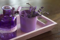 Lavanda in vasino lilla e bottiglia lilla in tavoletta su tavolo di legno — Foto stock