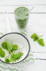 Bicchiere di frullato verde con ortica pungente in colino su legno bianco — Foto stock