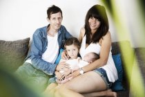 Young family with male newborn and little daughter sitting on sofa at home — Stock Photo