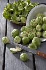 Bowl of Brussels sprouts with peels and knife on grey wooden table — Stock Photo