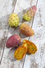 Sliced and whole prickly pears (Opuntia ficus-indica) on white wooden table, studio shot — Stock Photo