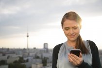 Young woman on rooftop terrace, using mobile phone — Stock Photo