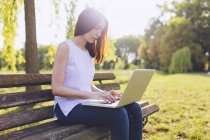 Женщина учится за ноутбуком, сидя на скамейке в парке — стоковое фото