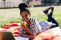 Mujer acostada sobre una manta en un prado comiendo manzana - foto de stock