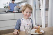 Niño comiendo gofres en la cocina - foto de stock