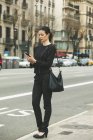 Giovane donna d'affari vestita di nero che telefona in strada — Foto stock