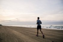 Junger Mann läuft am Sandstrand — Stockfoto