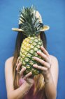 Женщина держит ананас перед лицом на синем фоне — стоковое фото