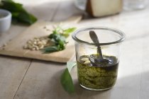 Pesto ramson fresco in un bicchiere, noci e foglie di basilico fresco su tavola di legno su sfondo — Foto stock