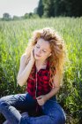 Porträt einer Frau, die in einem Feld sitzt und Musik mit Kopfhörern hört — Stockfoto