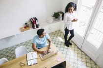 Joven hombre de negocios utilizando el ordenador portátil en la oficina y discutir con la mujer - foto de stock