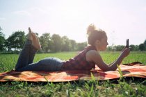 Donna con smartphone sdraiata su una coperta su un prato — Foto stock