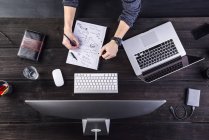 Homme travaillant au bureau avec ordinateur et ordinateur portable prenant des notes sur une feuille de papier — Photo de stock
