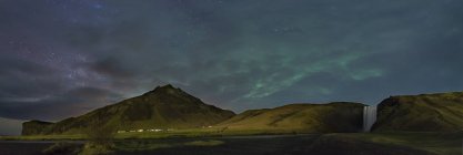 Islanda, aurora boreale e via lattea nella notte nuvolosa sul paesaggio panoramico con montagna e cascata — Foto stock