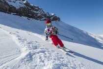 Мальчик в шлеме и лыжах в солнечный день на снежном склоне горы — стоковое фото