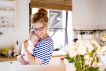 Счастливая мать с ребенком на кухне смотрит на ноутбук — стоковое фото
