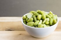 Edamame beans in small bowl on wooden chopping board — Stock Photo