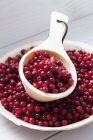 Wooden spoon and bowl with cranberries on white wooden table — Stock Photo