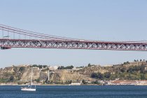 Portugal, Lisbon, View of 25 de Abril Bridge at River Tagus and floating yacht — Stock Photo