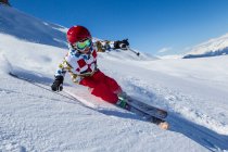 Boy in helmet and skiwear skiing in sunny day on snowy mountain slope — Stock Photo