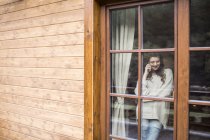 Young woman standing at the window using smartphone — Stock Photo