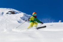 Boy in helmet and skiwear skiing in sunny day on snowy mountain slope — Stock Photo
