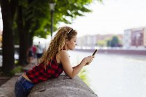 Itália, Verona, mulher à beira do rio a olhar para o telemóvel — Fotografia de Stock