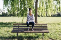 Portrait of young woman sitting on backrest of park bench — Stock Photo