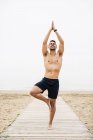 Jovem praticando ioga no calçadão na praia — Fotografia de Stock