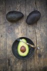 Ganze und halbierte Avocados auf dunklem Holz mit Teller und Gabel — Stockfoto