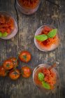 Bicchieri di granita di pomodoro guarniti con foglie di basilico e pomodorini su legno scuro, vista dall'alto — Foto stock