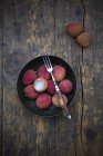Bowl of fresh litchis with fork on dark wood — Stock Photo