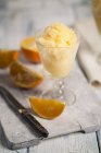 Vaso de granita naranja, cuchillo de cocina y trozos de naranja sobre tabla de madera - foto de stock